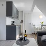 Küche, Essbereich und Wohnbereich mit dunklem Sofa und Wein auf Tisch.
