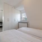 Schlafzimmer mit Bett, Kleiderschrank und Fenster. Im Hintergrund Wohnbereich mit Sofa.