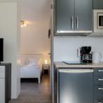 Küche mit Kühlschrank, Mikrowelle und Kaffeemaschine. Blick in Schlafzimmer mit Bett und Fernseher.