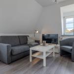 Wohnzimmer mit Sofa, Sessel, Couchtisch und TV. Holzboden und Fenster mit Blick.