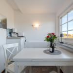 Weißer Tisch mit Stühlen, Fenster, Blumen und Getränke.