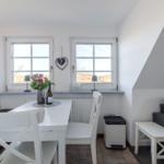 Essbereich mit weißem Tisch, Stühlen und Fenstern. Sofa und Fensterbank sichtbar.
