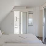 Schlafzimmer mit Dachschräge, Bett, Bad und Tür zum Flur.