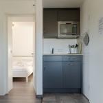 Küche mit Dunstabzug und Mikrowelle. Schlafzimmer mit weißem Bett im Hintergrund.