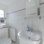 Badezimmer mit Waschbecken, Spiegel und Fenster mit Blick auf Häuser.