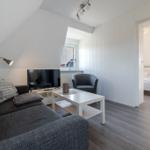 Wohnbereich mit Sofa, Fernseher und Sicht auf Schlafzimmer.