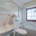 Badezimmer mit Dusche, Waschbecken und Toilette. Fenster mit Rollladen.