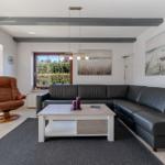 Wohnzimmer mit schwarzer Couch, brauner Sessel und Holztisch.
