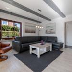 Wohnzimmer mit braunem Sessel, schwarzer Couch und Holzboden.
