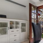 Weißer Schrank mit Glasfronten und dunkler Stuhl vor Fenster