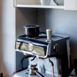 Espresso-Maschine mit Milchkanne und Tassen auf Küchenregal.