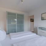 Schlafzimmer mit weißem Bett, Schrank und Spiegelschrank