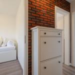 Zimmer mit weißem Bett und Backsteinwand. Schrank und Türen zu weiteren Räumen.