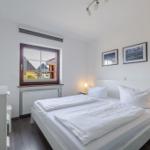 Schlafzimmer mit weißem Bett, Fenster und Nachttischen.