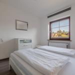 Schlafzimmer mit Doppelbett, Fenster und Spiegel an der Wand.