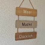 Drei Holztafeln hängen an einem Seil an der Wand. Sie zeigen die Worte Meer, Macht und Glücklich.