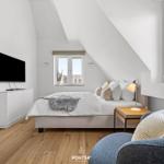 Schlafzimmer mit Bett, Fernseher und Sessel. Holzboden und große Fenster.