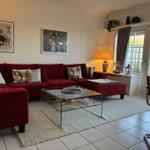 Ein Wohnzimmer mit rotem Sofa, Glas-Tisch und Blick auf einen Garten.