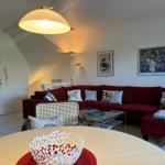 Ein Wohnzimmer mit rotem Sofa, Glas-Tisch und Wandbildern.