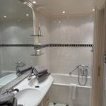 Badezimmer mit Badewanne, Waschbecken und Spiegel. Fliesen und Handtücher sind sichtbar.