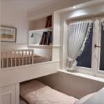Zimmer mit Doppelstockbett, Bücherregal und Fenster mit weißen Vorhängen.
