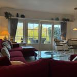 Ein Wohnzimmer mit rotem Sofa, Glas-Tisch und Fenstern zum Garten.