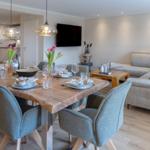 Esszimmer mit Esstisch und Stühlen. Wohnzimmer mit Sofa und Fernseher. Holzboden und Pendelleuchten.
