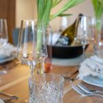 Gestellte Tischdekoration mit Tulpen, Gläsern und Geschirr auf Holztisch.