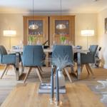 Esszimmer mit Holztisch, blauen Stühlen und Glaswand-Schrank. Holzboden und Wandbild.