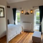 Schlafzimmer mit Holzboden, Bett, zwei Fenster und Sitzbank.