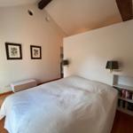 Schlafzimmer mit Bett, Bücherregal und Wandlampen. Holzboden und schräge Decke mit Balken.
