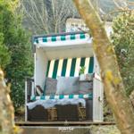 Ein Strandkorb mit grün-weißem Streifenmuster und Kissen im Garten.