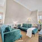 Ein Wohnzimmer mit grünem Sofa, Holzboden und großen Fenstern.