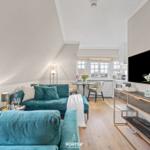 Wohnzimmer mit Sofa, Fernseher und Essbereich. Holzboden und großes Fenster.