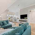 Wohnbereich mit Sofa, Fernseher und Küche im Hintergrund.