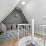 Dachbodenwohnung mit Sitzbank, weiße Wendeltreppe und Holzboden.