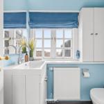 Badezimmer mit blauen Wänden, weißem Waschbecken und Fenster mit blauem Rollladen.