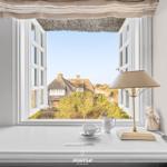 Weißer Fensterbalken mit Tasse, Lampe und Blick auf strohgedecktes Haus.