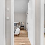 Schlafzimmer mit Bett, Nachttisch und Blumen. Holzboden und weiße Türen.