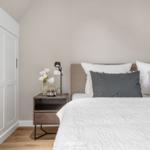 Schlafzimmer mit Bett, Nachttisch und Schrank. Wandfarbe beige, Boden aus Holz.