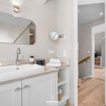 Badezimmer mit Waschbecken, Spiegel und Blick in den Flur.
