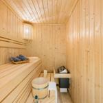 Sauna mit Holzbank, Eimer, Korb und Heizung.