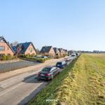Reihe von Häusern mit dunklen Dächern entlang einer Straße mit Parkplätzen und grünem Feld.