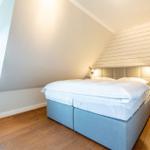 Schlafzimmer mit Doppelbett, Holzboden und Holzwand. Fenster mit Tischlampe.