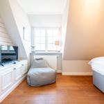Schlafzimmer mit Bett, Sitzgelegenheit und TV-Anlage unter Dachschrägen.