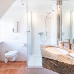 Badezimmer mit Dusche, Waschbecken und Toilette unter Dachschräge.