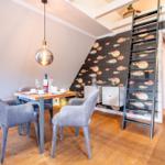 Essbereich mit Tisch, Stühlen und Wand mit Fischmotiv. Treppenhaus mit Leiter führt zur oberen Etage.