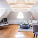 Wohnraum mit Holzboden, Sofa, Sessel und runden Tisch unter Holzbalkendecke.