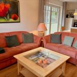 Zwei orangefarbene Sofas mit Kissen um einen Holztisch mit Glasplatte.