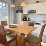 Essbereich mit Holztisch und Stühlen. Küche mit weißen Schränken und Arbeitsfläche.